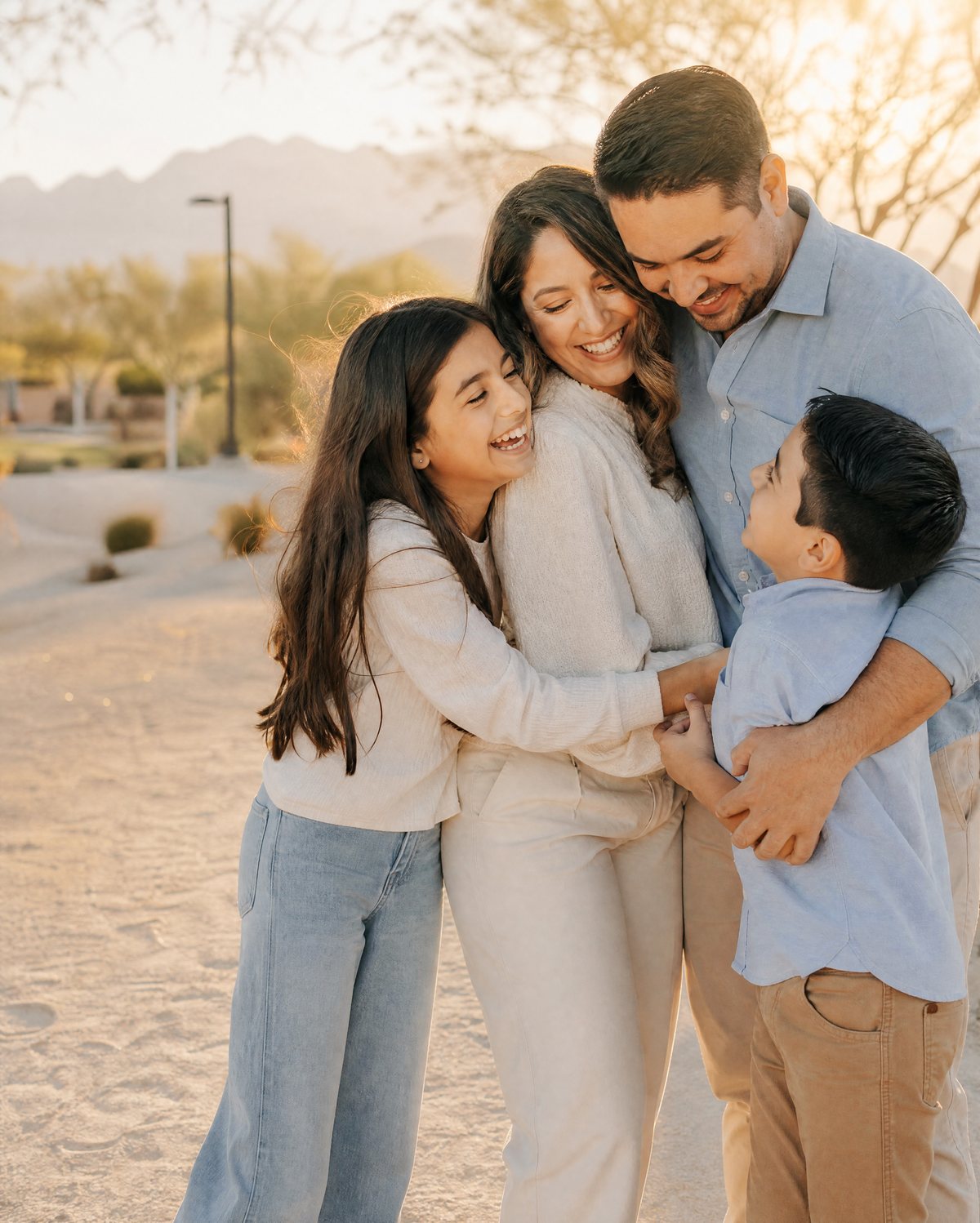 A smiling family of four hugging in a Southwest Las Vegas park at sunset